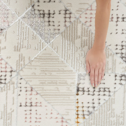 Cream geometric patchwork rug with diamond motifs in grey, beige and blush; soft woven texture, hand resting on it.