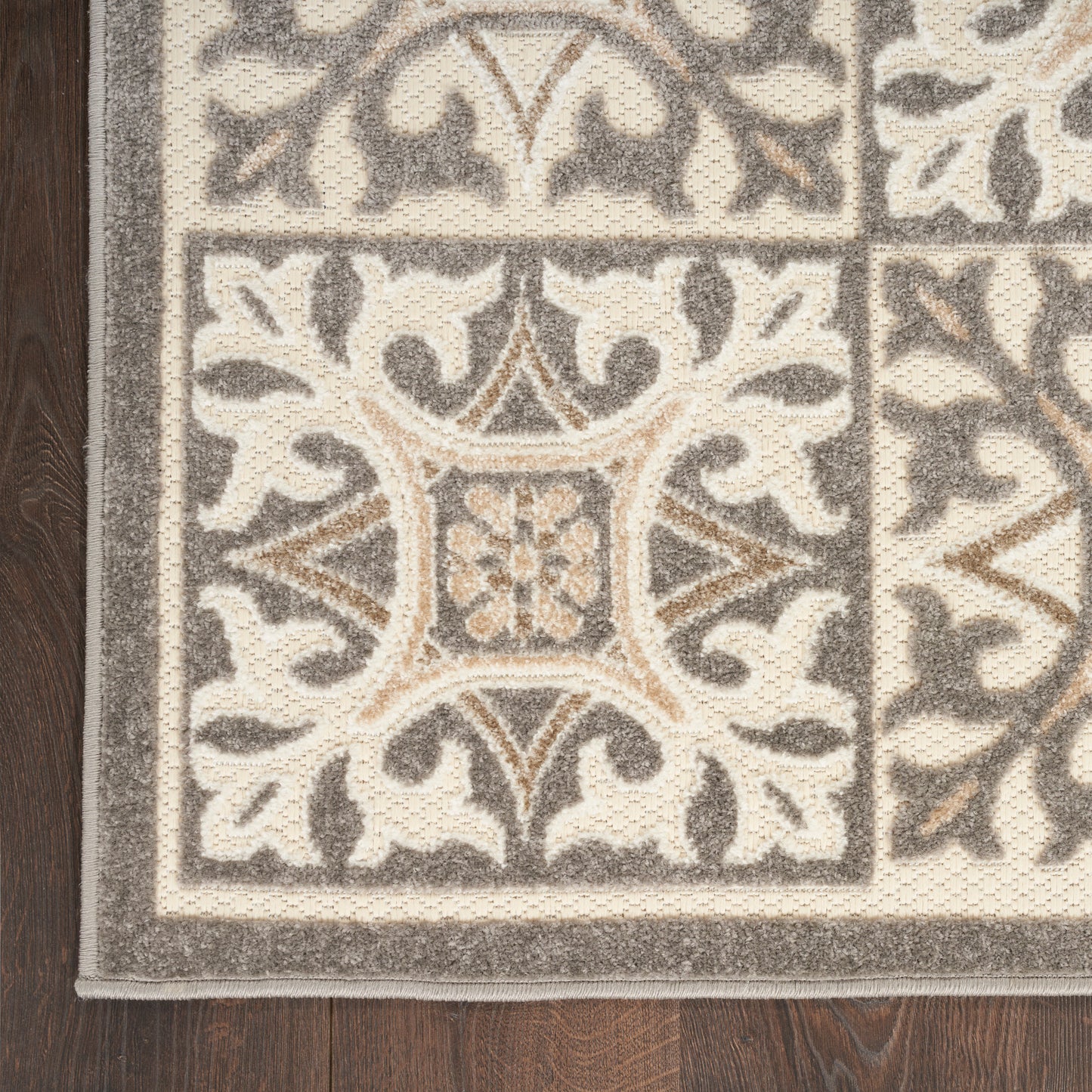 Beige and grey ornate patterned area rug with damask tile motif, textured pile, bordered in light grey, on dark wood floor