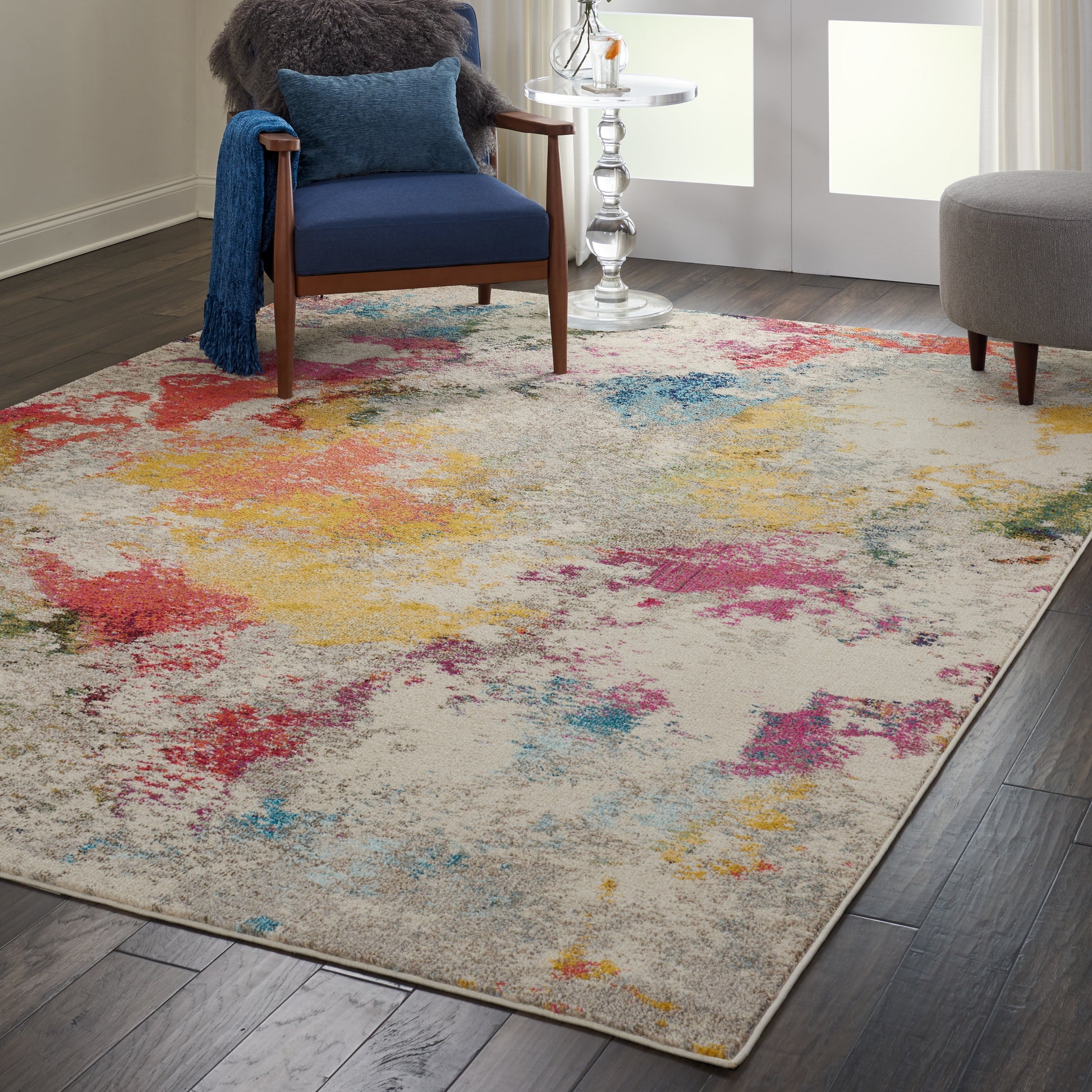Rectangular plush area rug with a beige base and multicolor blotches of red, yellow, blue; pairs with navy chair.