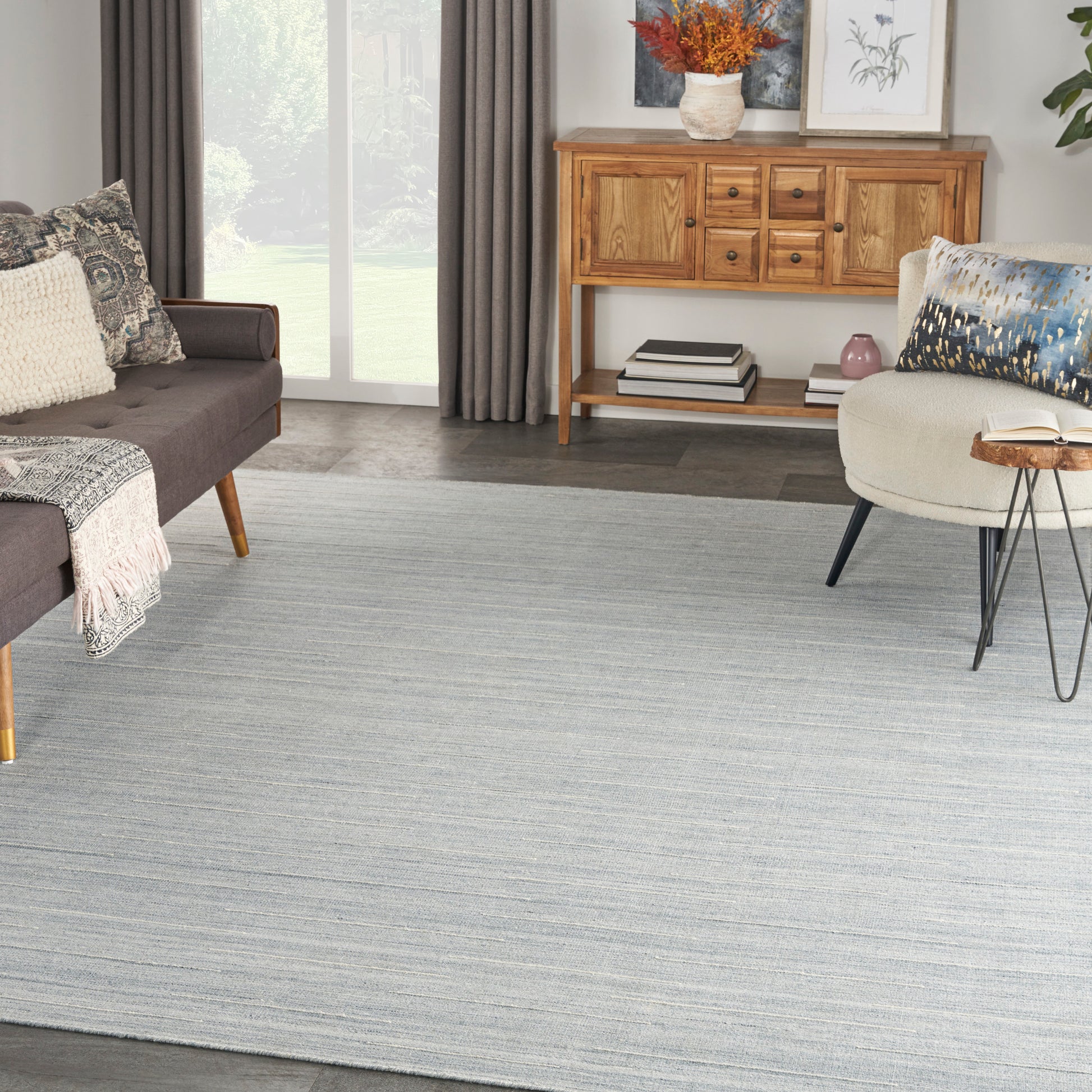 Living room with light gray-blue striped rug, brown fabric sofa, beige throw, wooden sideboard, and an armchair.