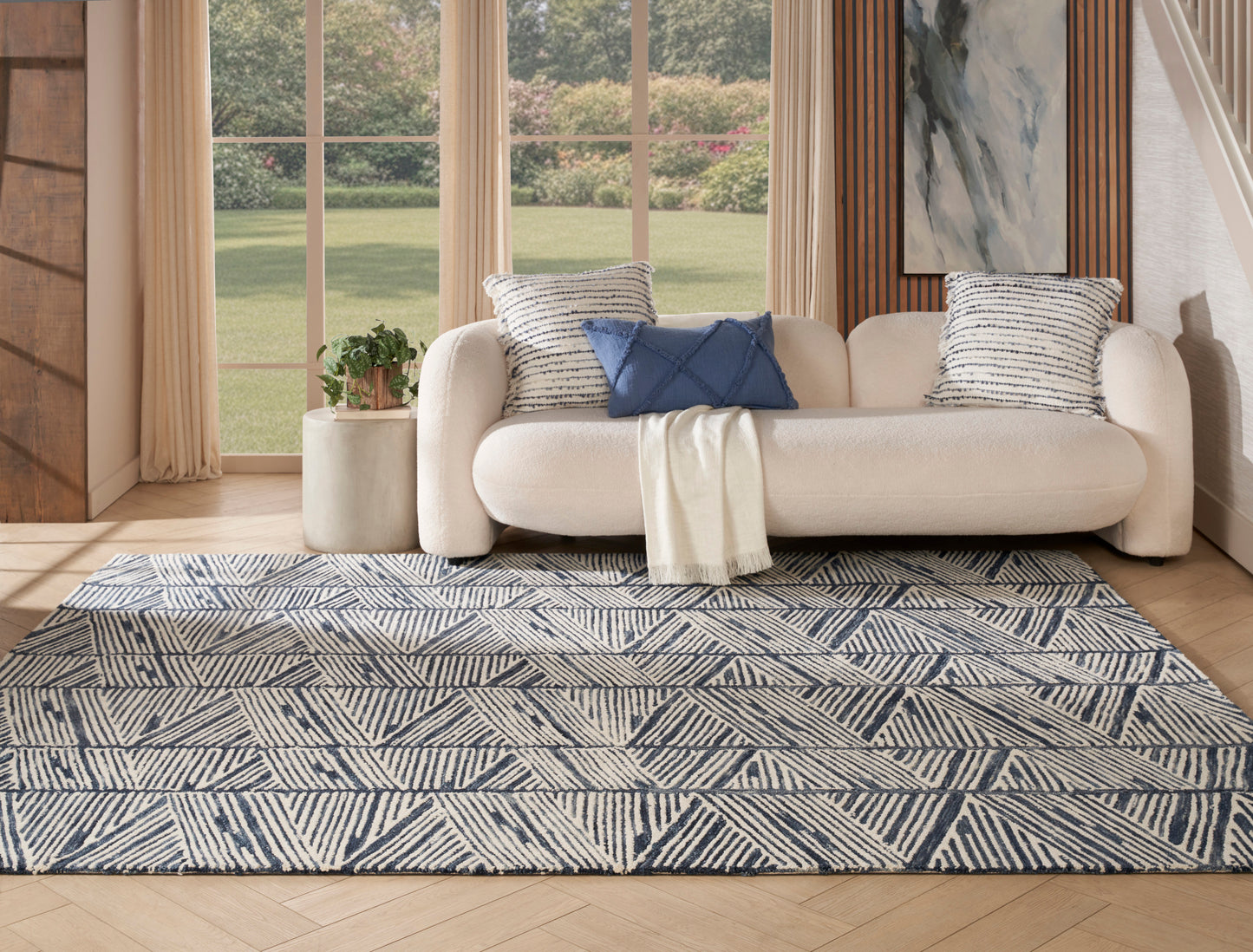 Cream fabric sofa with striped and navy cushions, cream throw, and a navy-ivory geometric rug in a bright living room.