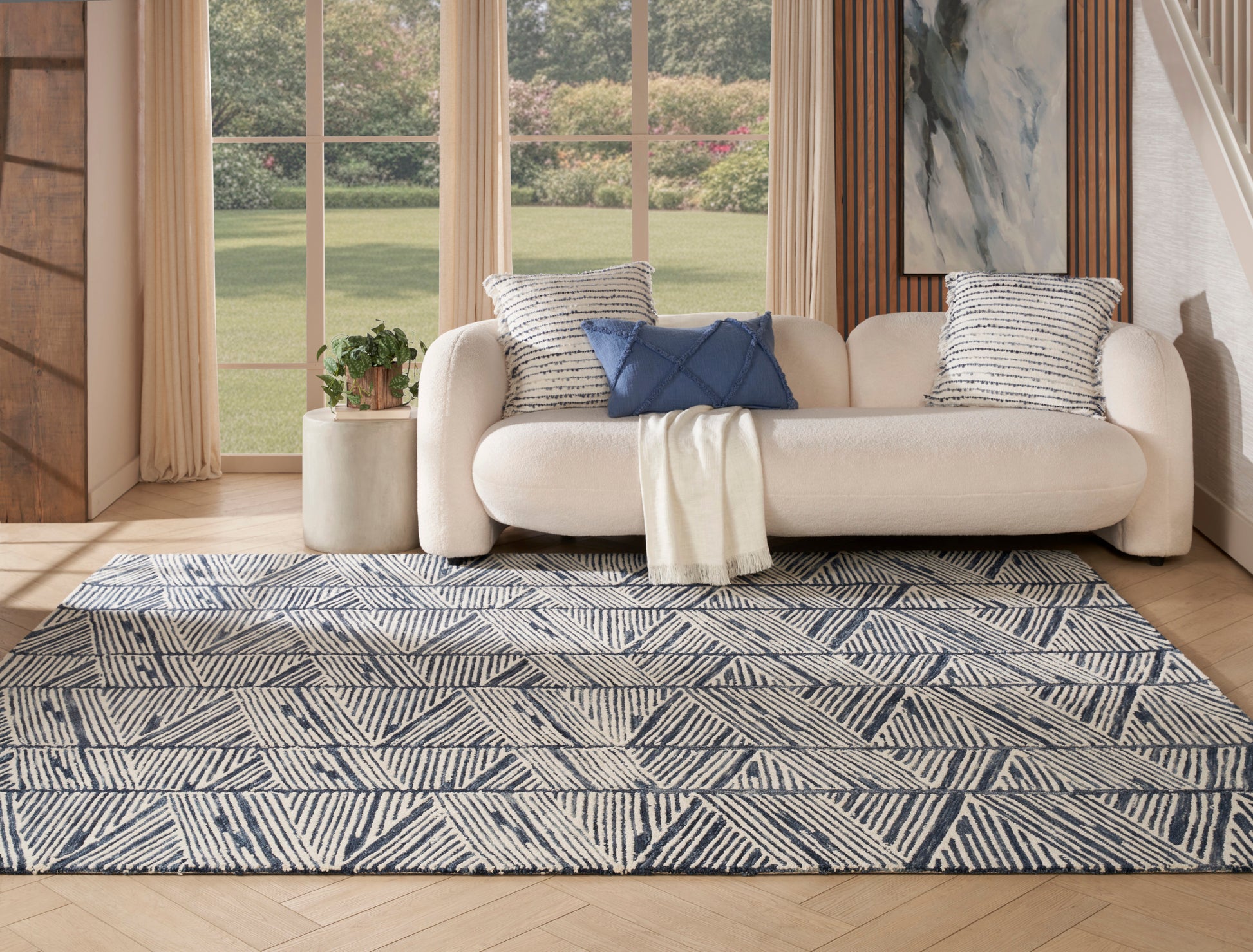 Cream fabric sofa with striped and navy cushions, cream throw, and a navy-ivory geometric rug in a bright living room.
