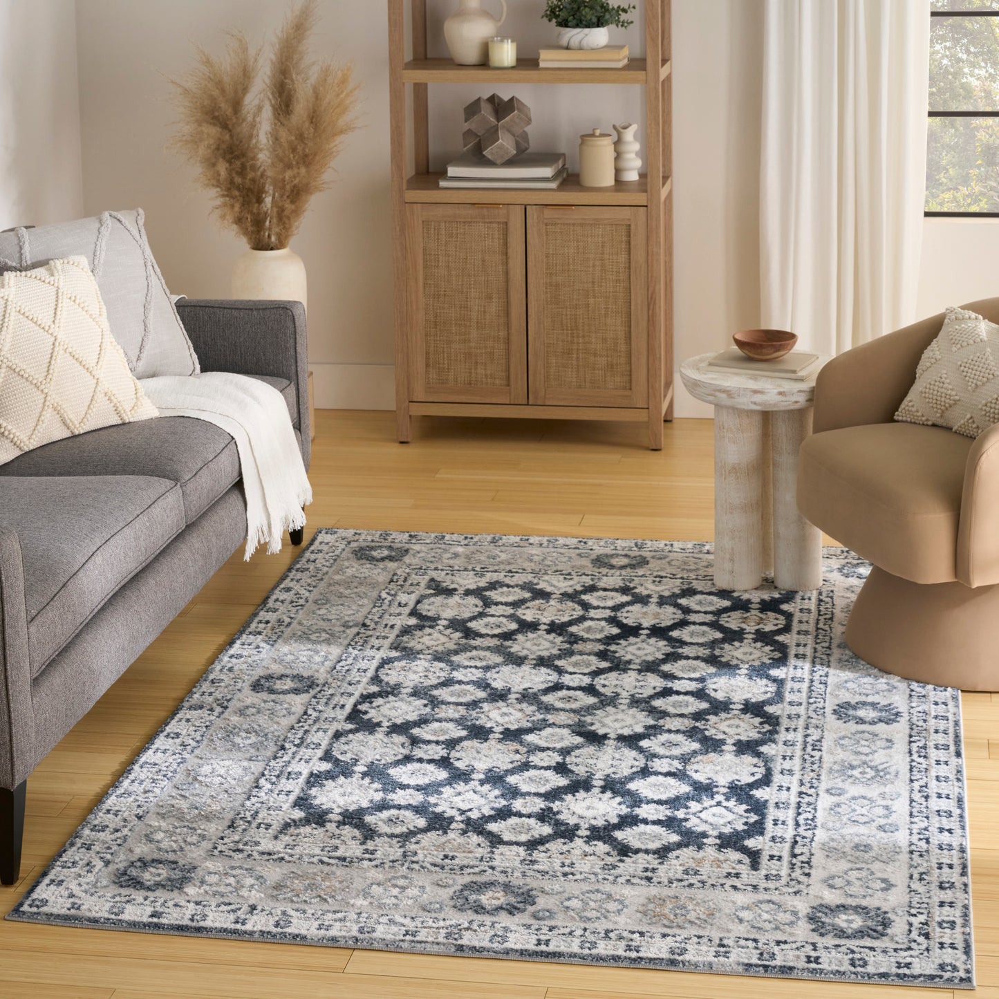 Blue and ivory woven area rug with a medallion border in a living room with a gray sofa and beige chair.