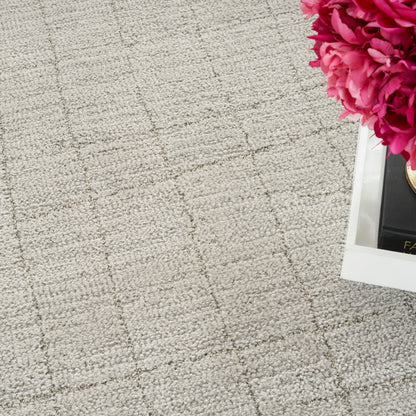 Beige textured rug with a subtle grid pattern and a white tray holding bright pink peonies in the top-right corner.