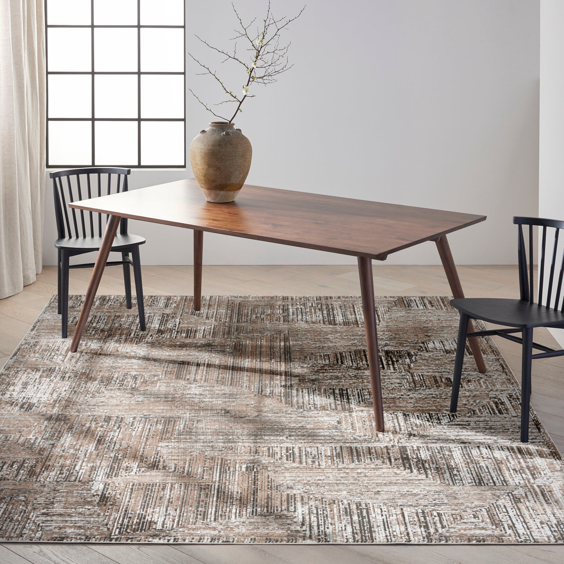 Mid-century wooden dining table with tapered legs, paired with black chairs, ceramic vase centerpiece on a textured beige rug.