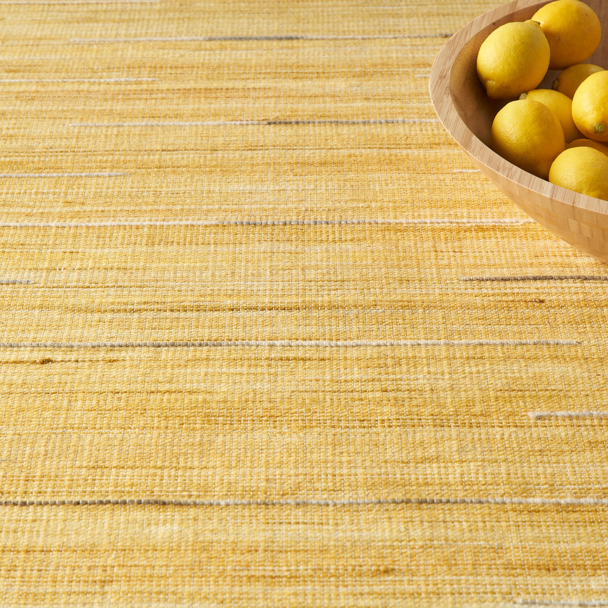 Golden-yellow woven rug (8' x 10') with a wooden bowl of lemons in the top-right.