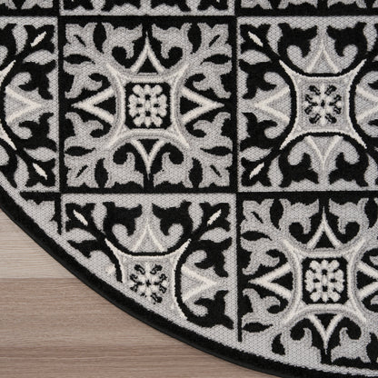 Round black & gray rug with tile-like square medallions and ornate floral scrollwork on wood floor.