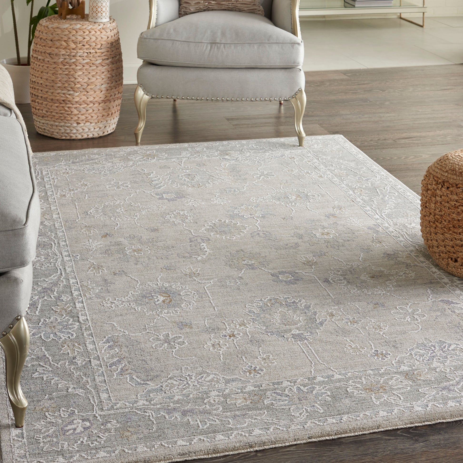 Light gray floral patterned area rug on wood floor, paired with gray upholstered chairs and woven basket stools.