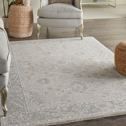 Light gray floral patterned area rug on wood floor, paired with gray upholstered chairs and woven basket stools.