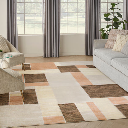 Geometric color-block rug in cream, peach, tan & brown on light wood floor, gray sofa, beige chair, windows & plant.
