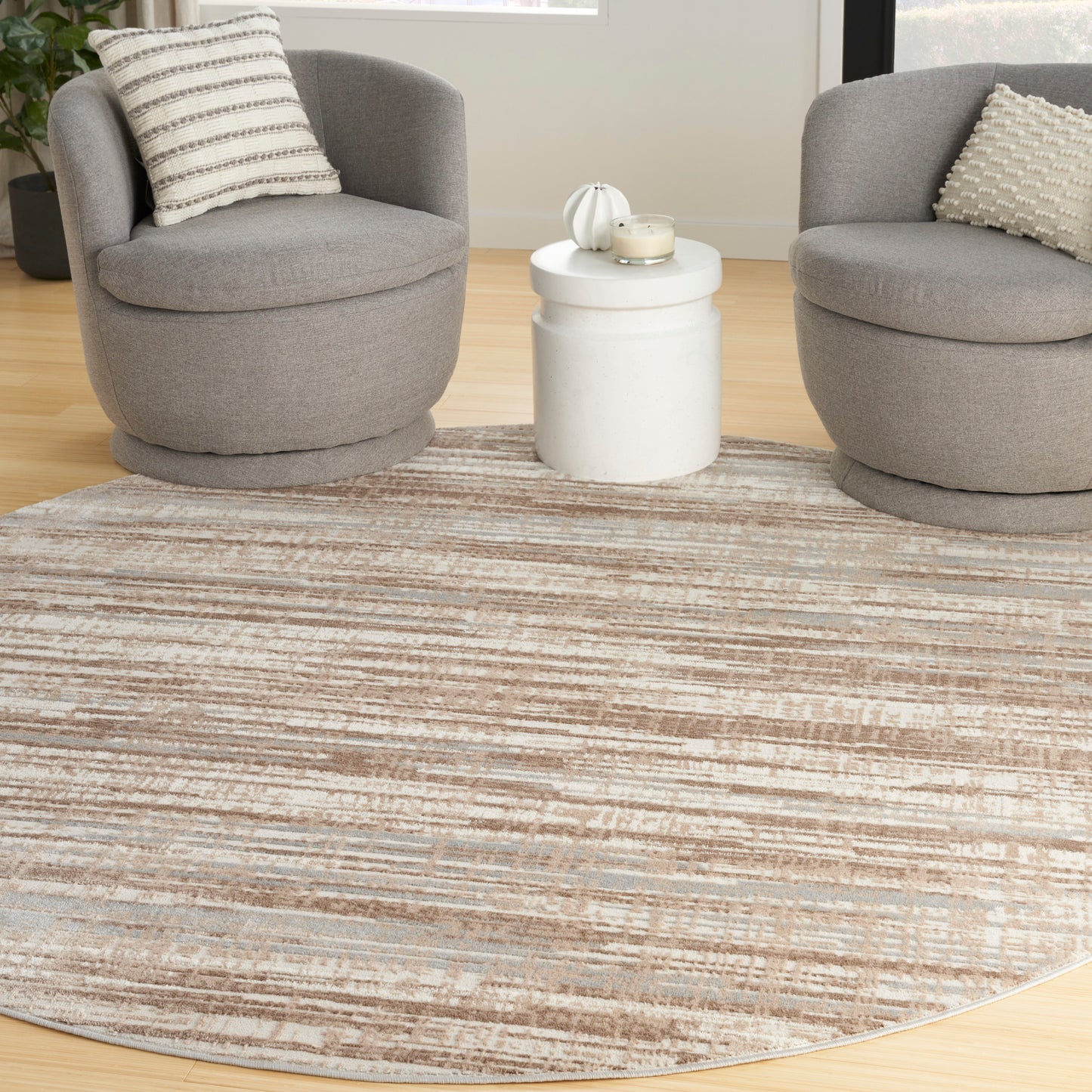 Round beige-taupe striped area rug between two grey circular lounge chairs and a white side table.