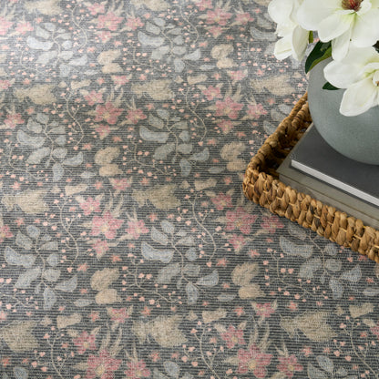 Floral gray-pink woven rug with vine pattern; wicker tray, gray vase, white flowers, and books.