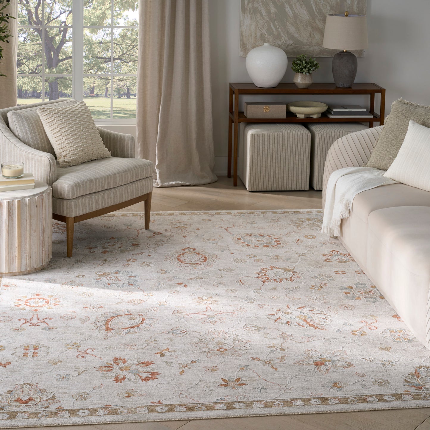Bright neutral living room with cream sofa and armchair, light floral area rug, and a wooden console shelf with decor.