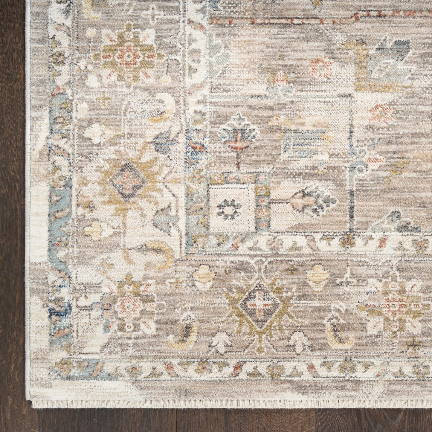 Vintage-style floral area rug in ivory, taupe, blue and gold with a distressed pattern and fringe edge on dark wood floor