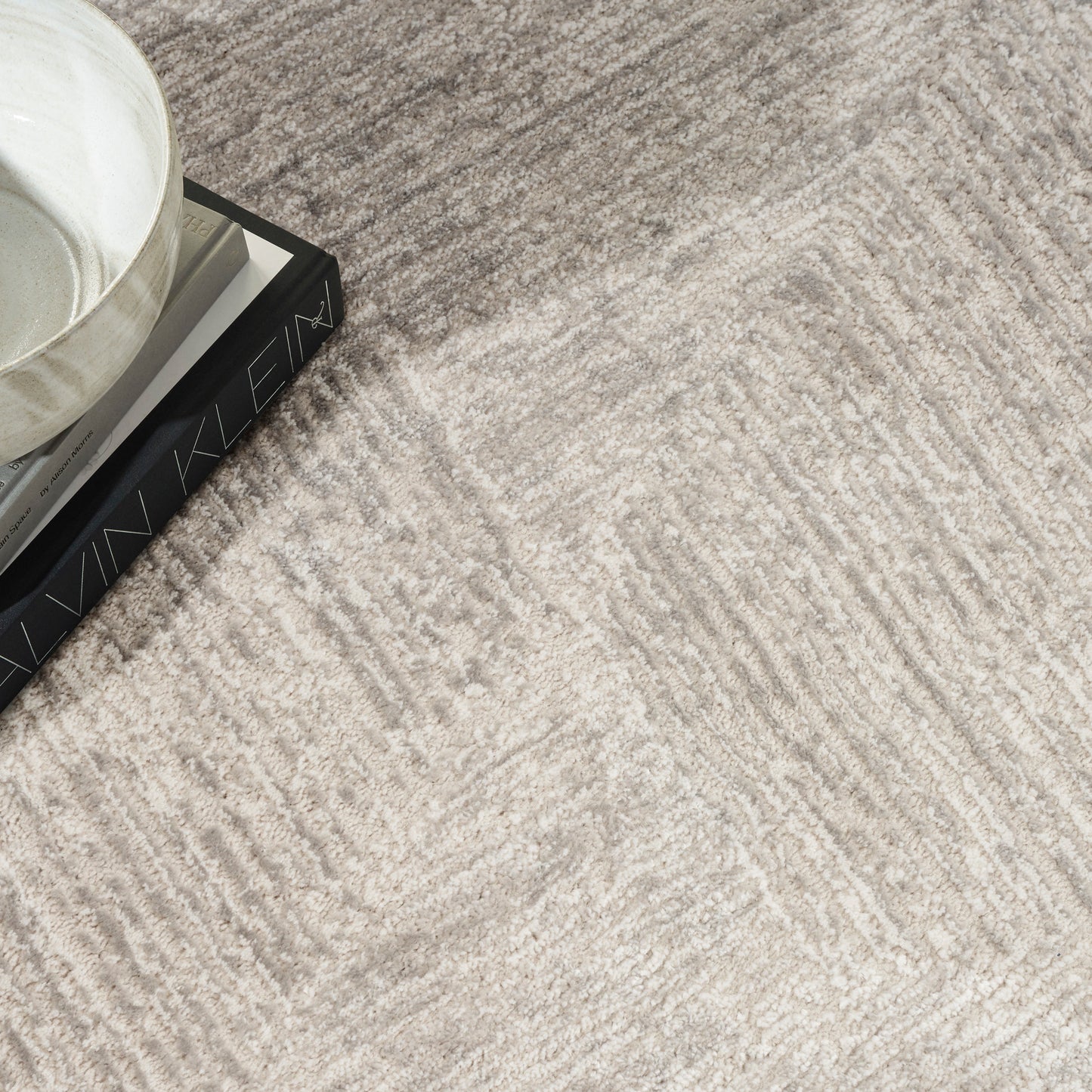 Beige textured rug with cream pattern; white ceramic bowl on a dark book.