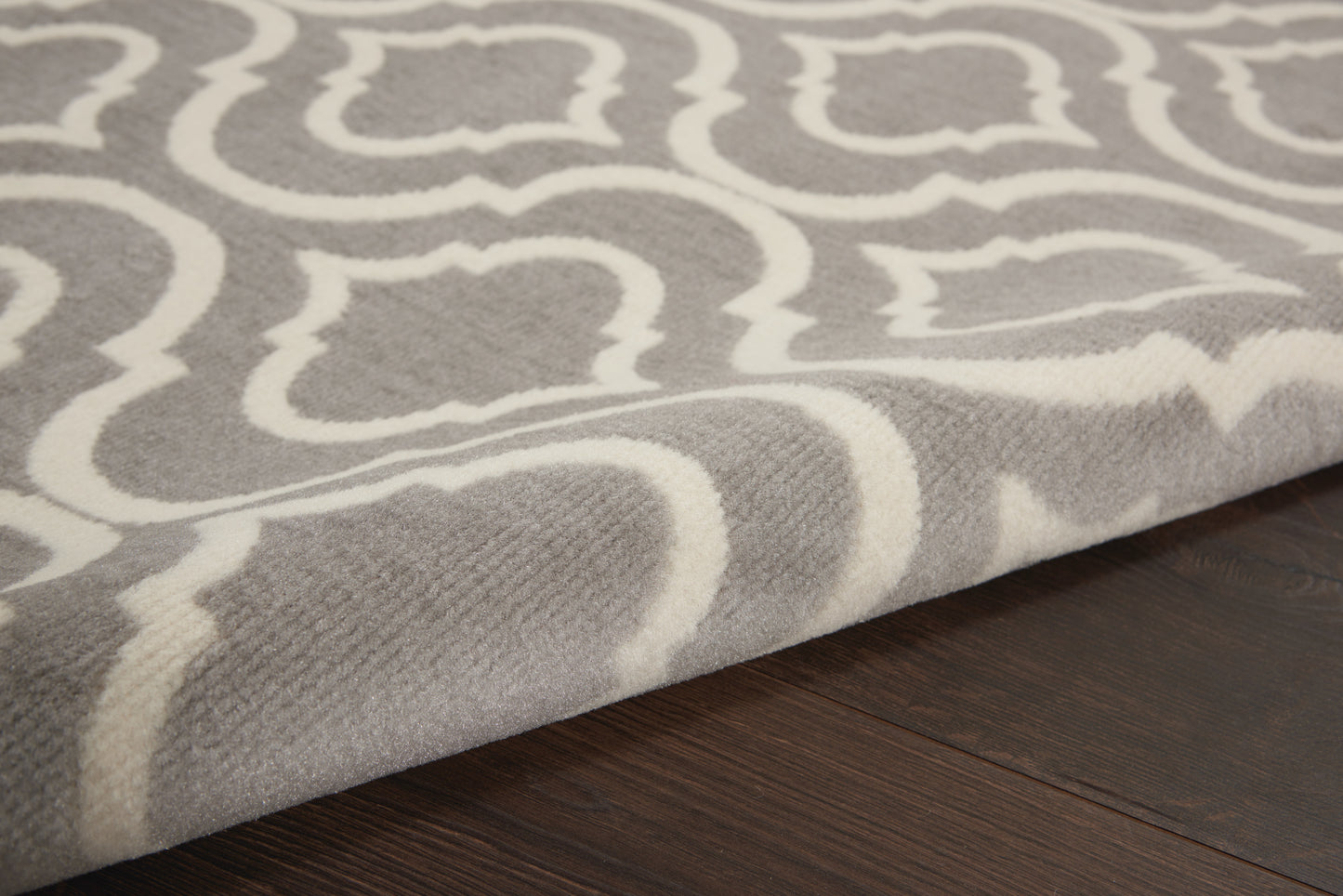 Grey and white geometric patterned area rug with woven texture on dark wooden floor.