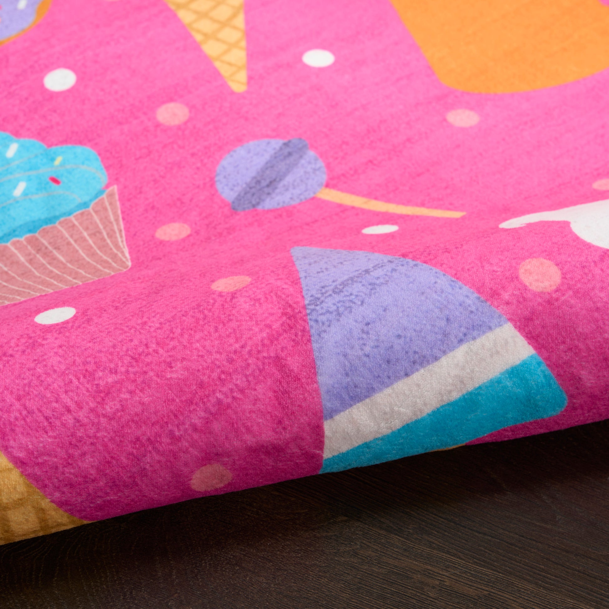 Bright pink rug with a colorful dessert print featuring a blue-frosted cupcake, an ice cream cone and candy shapes.
