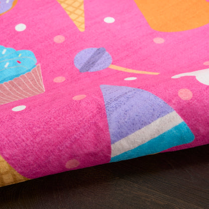 Bright pink rug with a colorful dessert print featuring a blue-frosted cupcake, an ice cream cone and candy shapes.