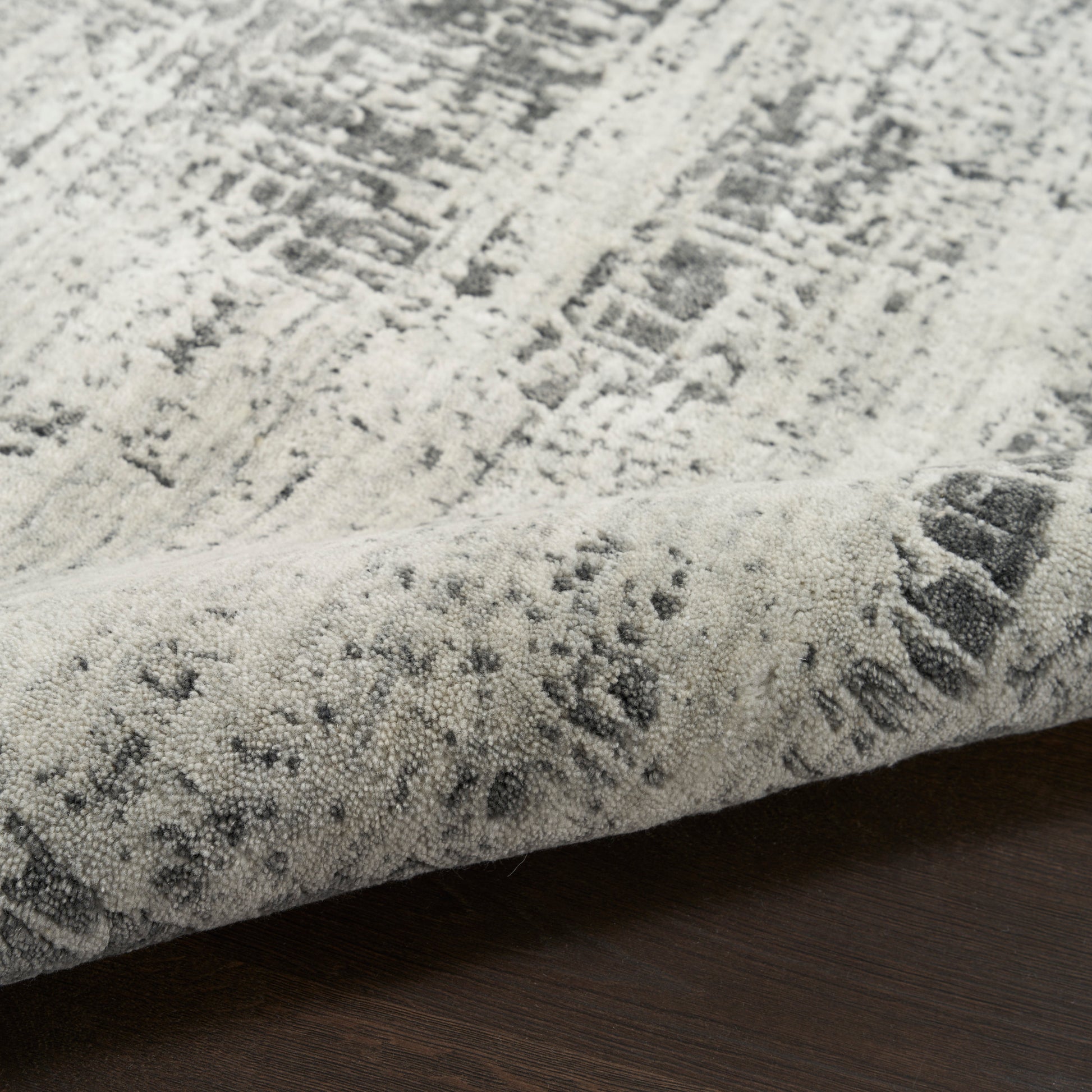 Light gray and white abstract area rug with distressed pattern, low-pile, rolled edge on dark wood floor.