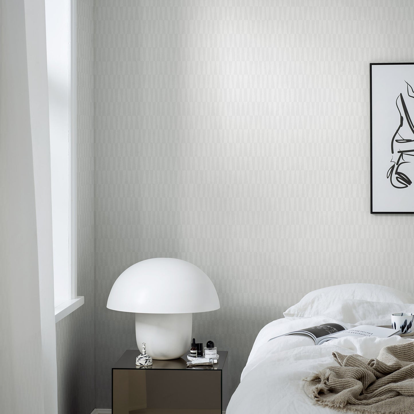 White mushroom-shaped table lamp on a mirrored bedside table beside a white bed with a beige knit throw in a modern minimalist bedroom.