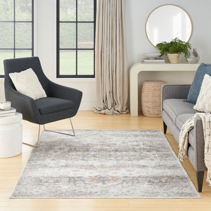 Vintage living room with a light gray-blue rug, gray chair, gray sofa, pillows, beige curtains, round mirror & wicker ottoman.