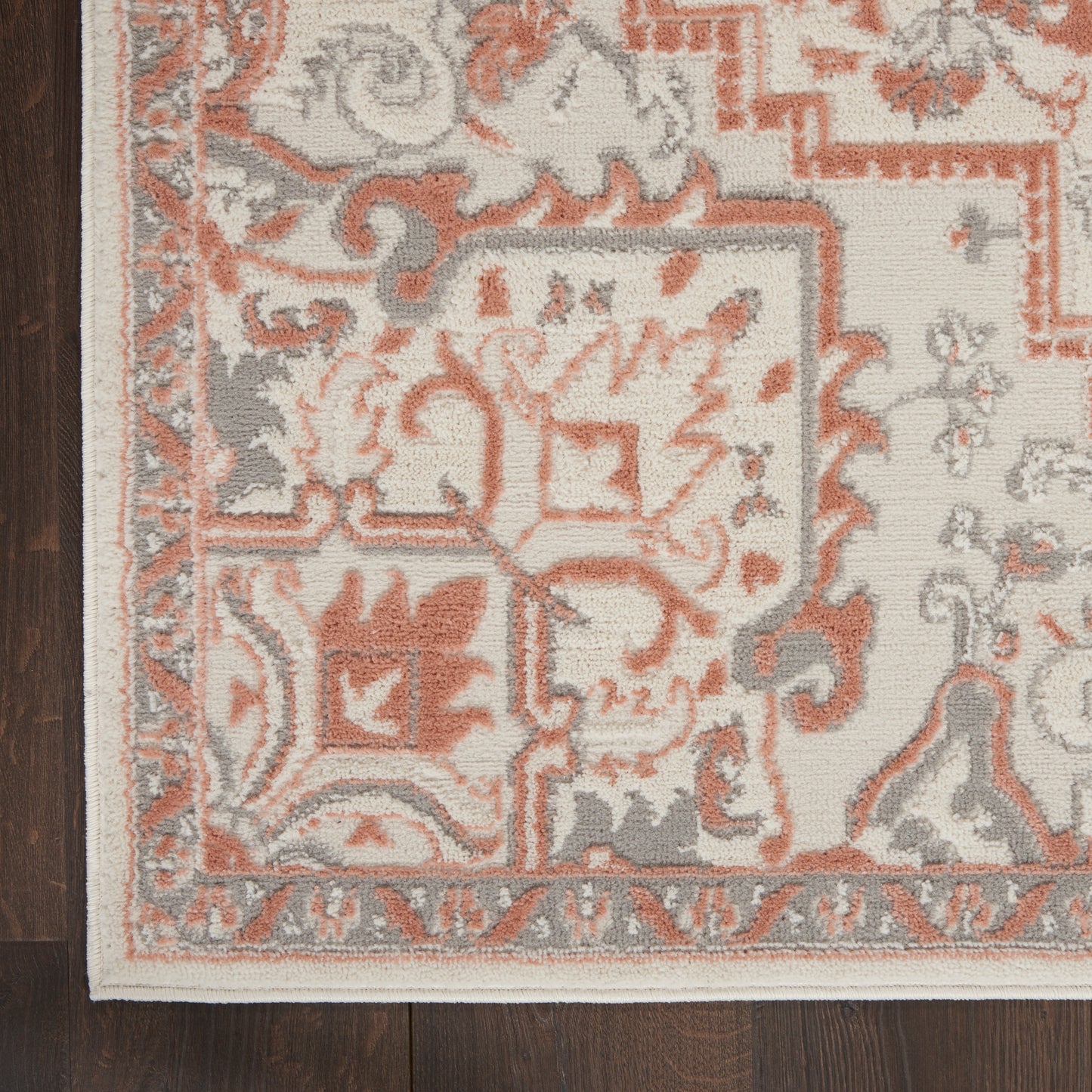 Cream and coral traditional Persian rug with gray accents, floral border and fringed edge on dark wood floor.
