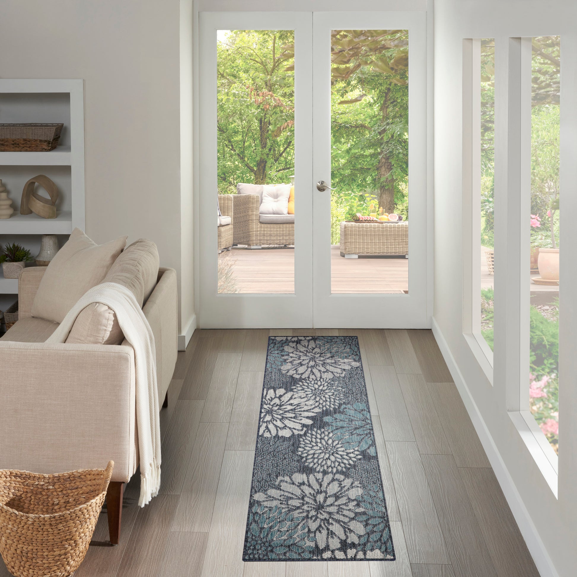 Long blue-gray floral runner rug on light wood floor beside beige sofa, in a bright living room with glass French doors.