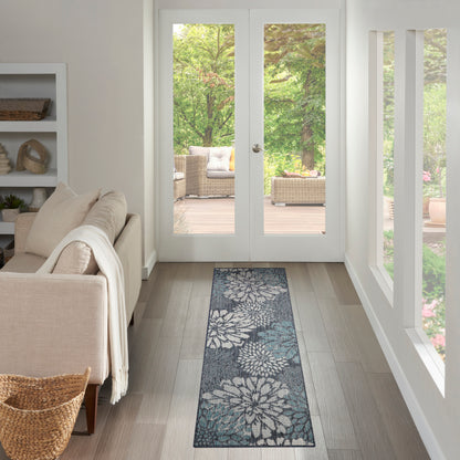 Long blue-gray floral runner rug on light wood floor beside beige sofa, in a bright living room with glass French doors.