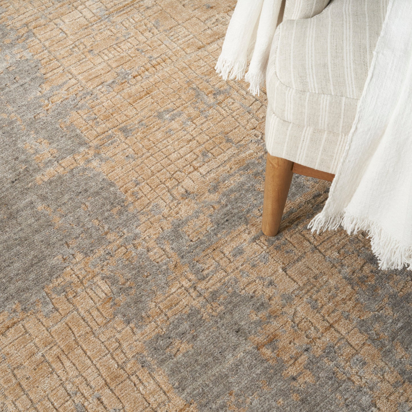 Beige-gray textured geometric rug with a white fringed throw draped nearby.