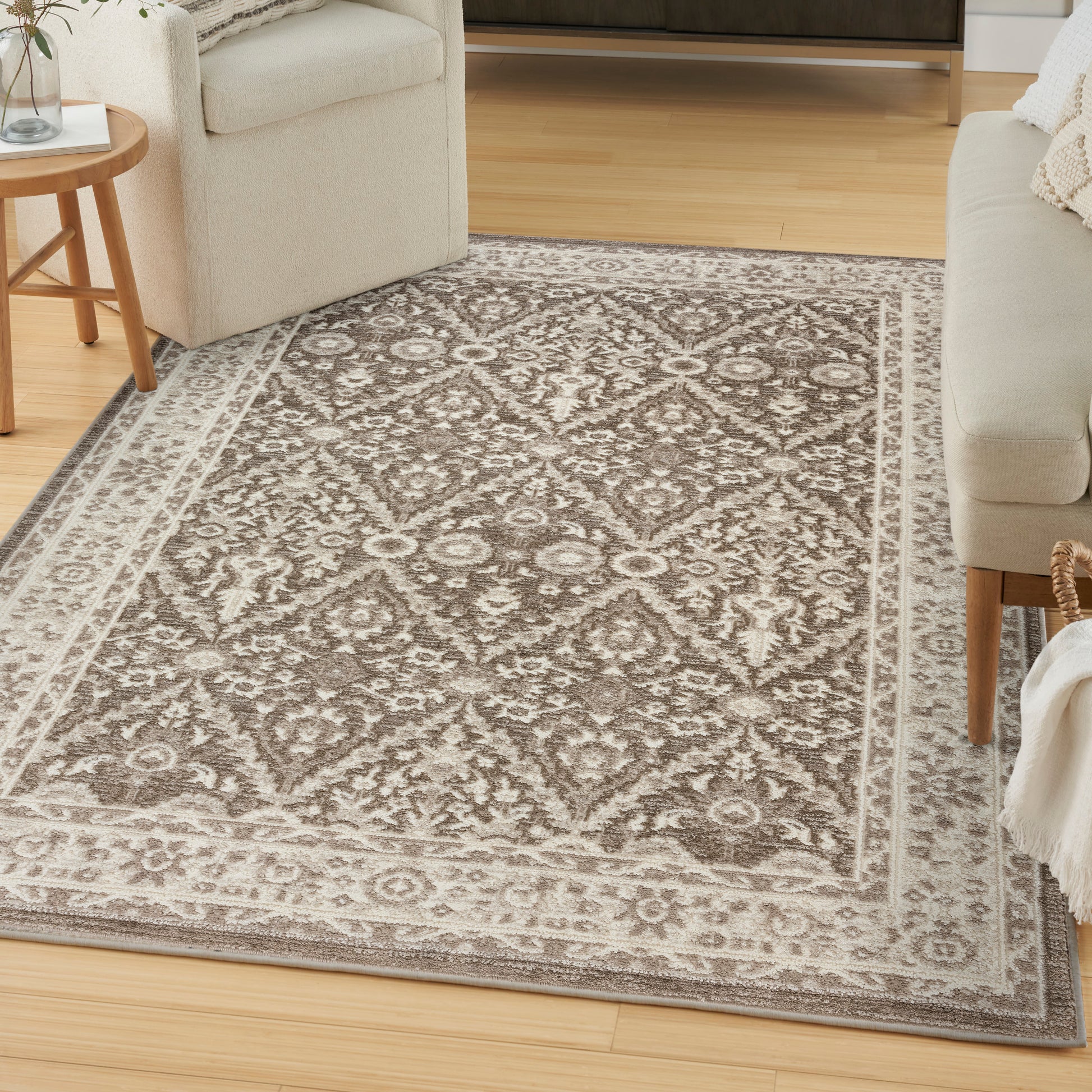 Taupe and ivory ornate area rug with medallion pattern and bordered edge; living room with light sofas and wooden furniture.