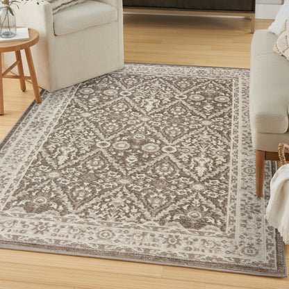 Taupe and ivory ornate area rug with medallion pattern and bordered edge; living room with light sofas and wooden furniture.
