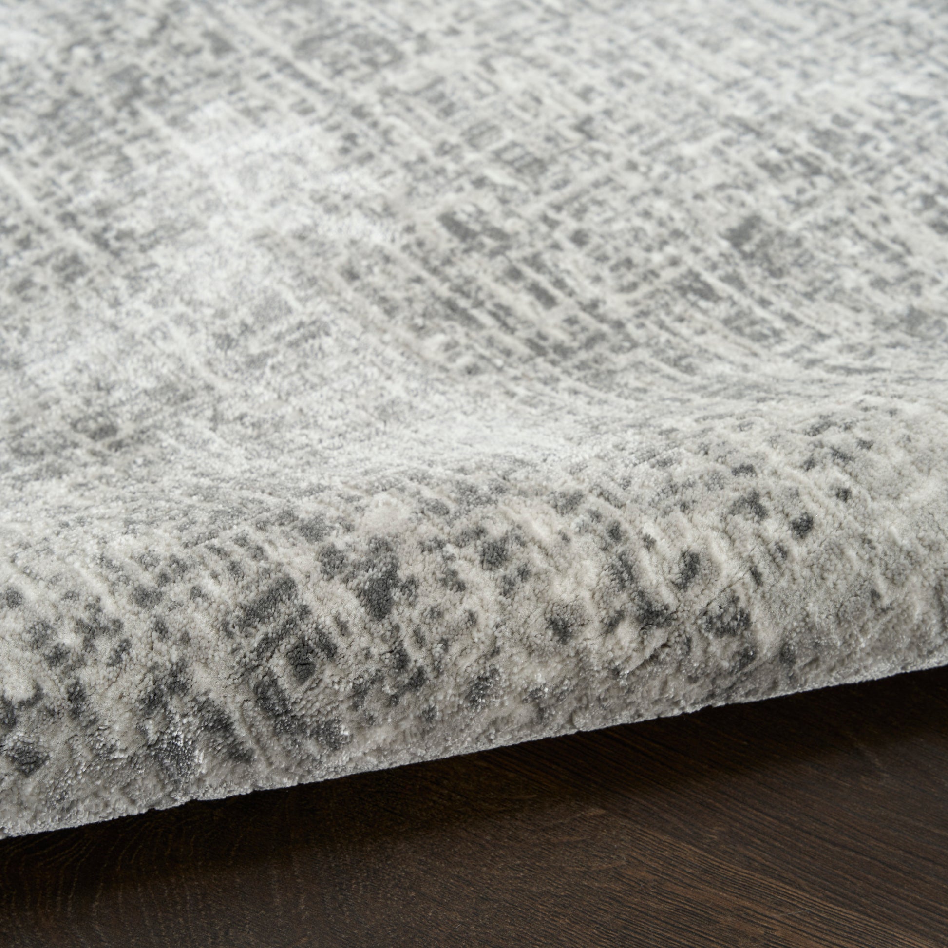 Grey abstract patterned rug with distressed, tonal design on a dark wood floor; soft, plush pile and rolled edge.