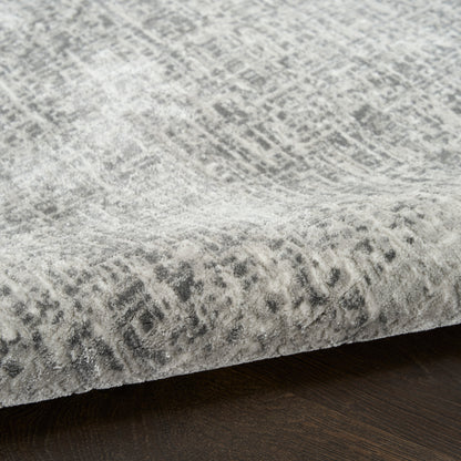Grey abstract patterned rug with distressed, tonal design on a dark wood floor; soft, plush pile and rolled edge.