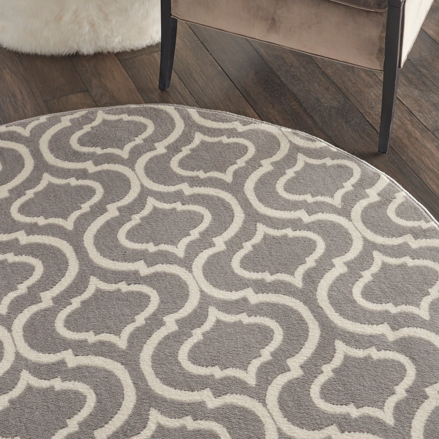 Round grey rug with white trellis geometric pattern on dark wood floor; contemporary living room.