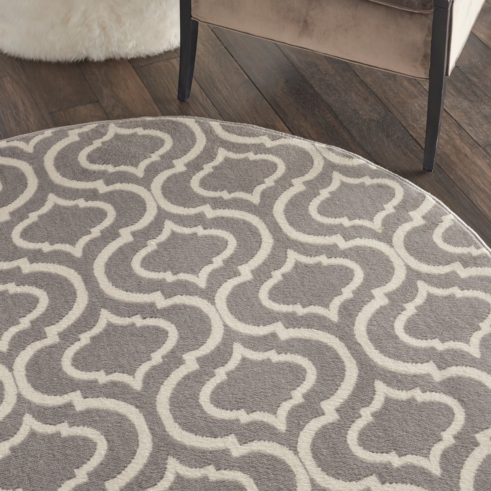 Round grey rug with white trellis geometric pattern on dark wood floor; contemporary living room.