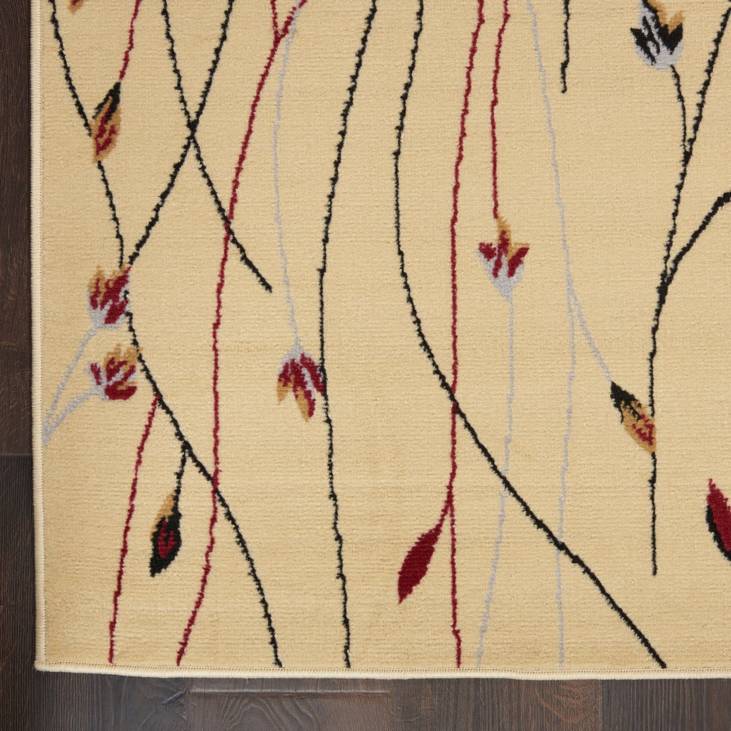 Beige rug with abstract black, red and pale blue curved lines and small burgundy leaf accents; fringe along edge.