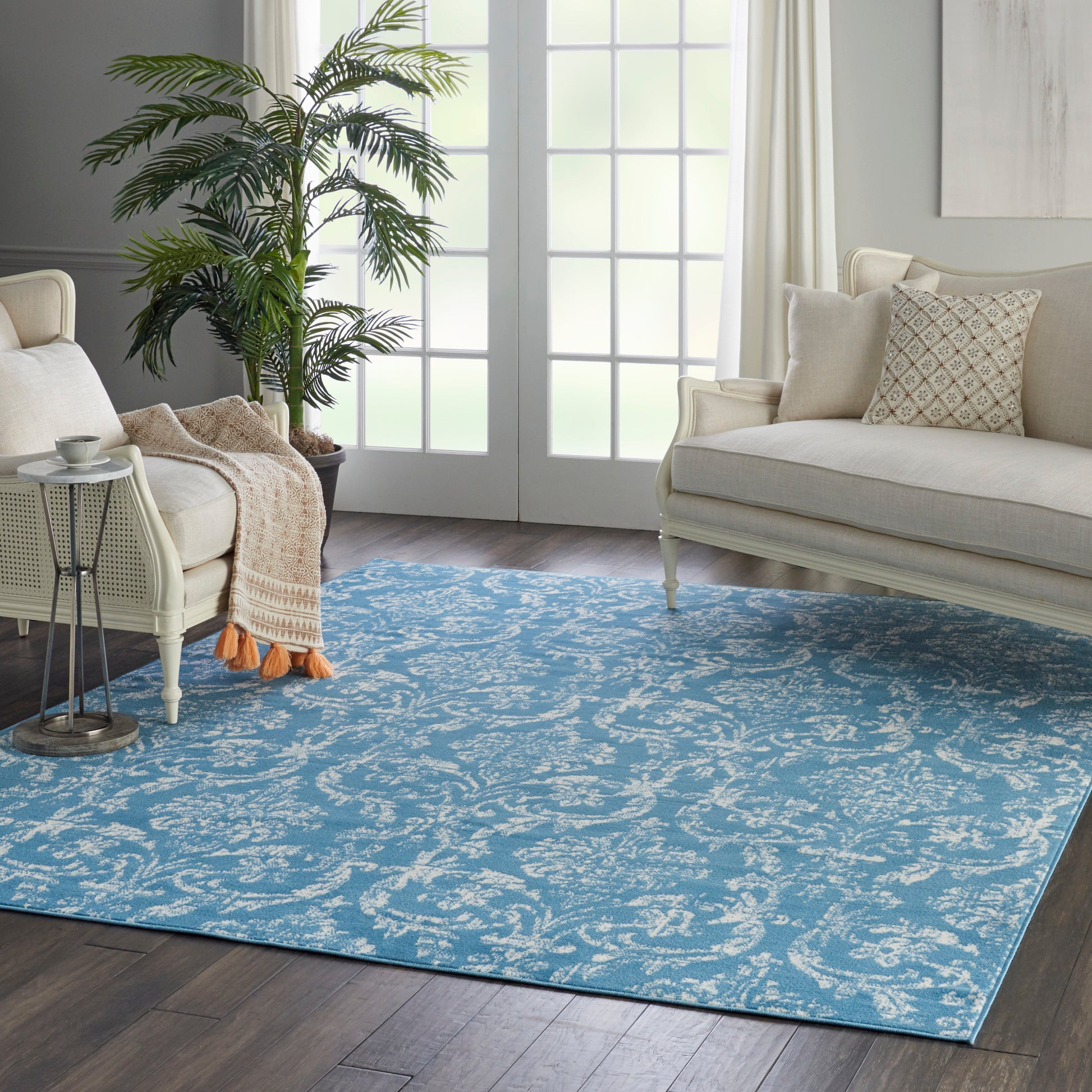 Blue and white patterned area rug in a bright living room with white sofas, a tall plant, and neutral decor.