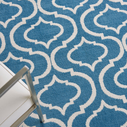 Blue rug with white trellis pattern; textured weave in modern geometric style, with part of white metal chair leg visible.