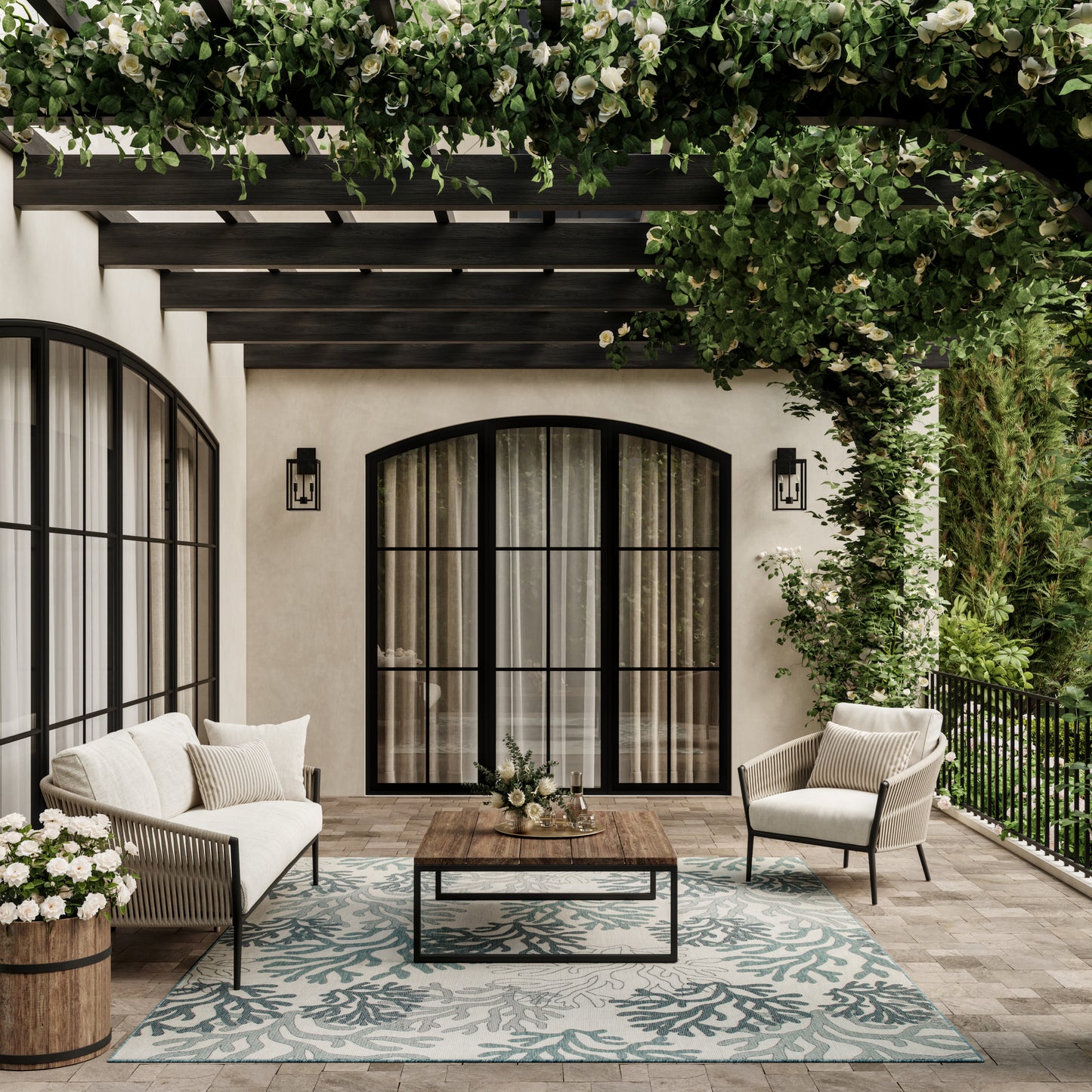 Outdoor patio with cream cushioned wicker seating, black arched doors, wooden coffee table, teal coral-pattern rug, and lush green vines.
