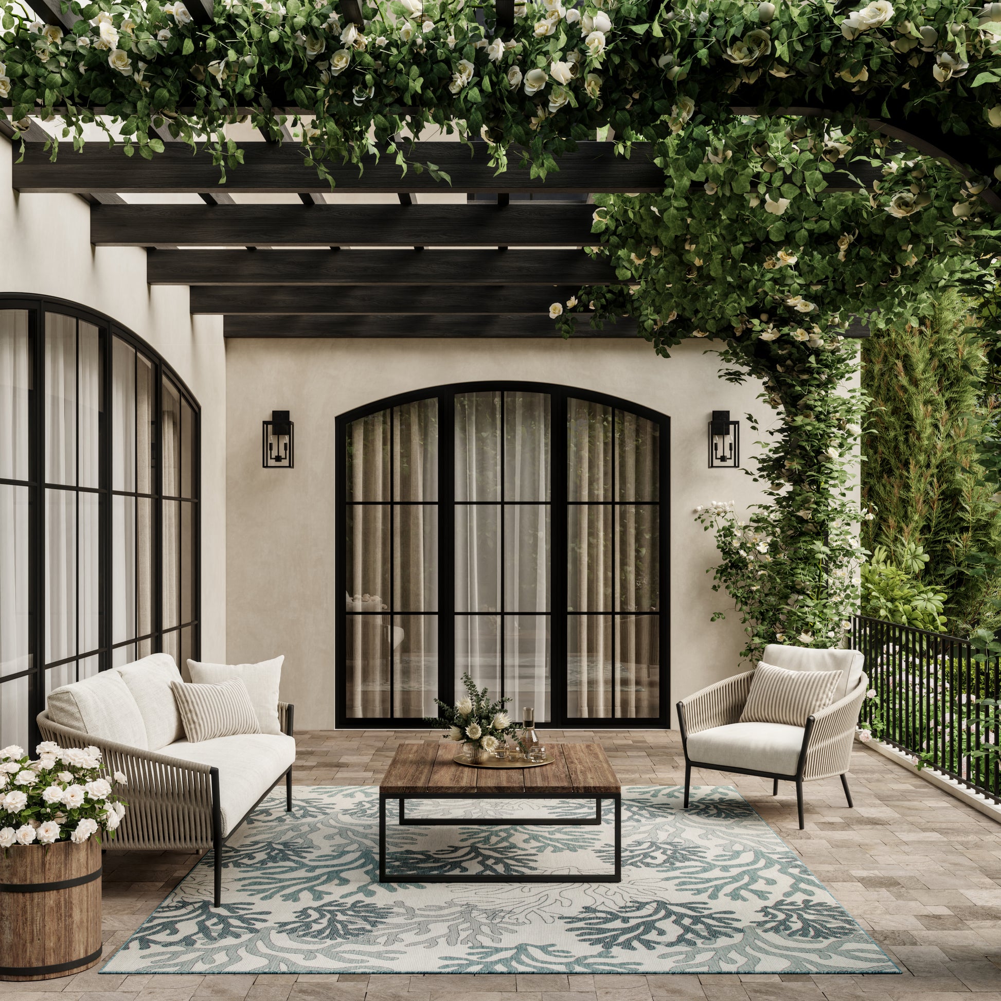 Outdoor patio with cream cushioned wicker seating, black arched doors, wooden coffee table, teal coral-pattern rug, and lush green vines.