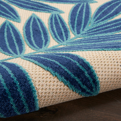 Close-up of a beige woven rug with bold blue leaf pattern and teal accents; natural fiber texture.