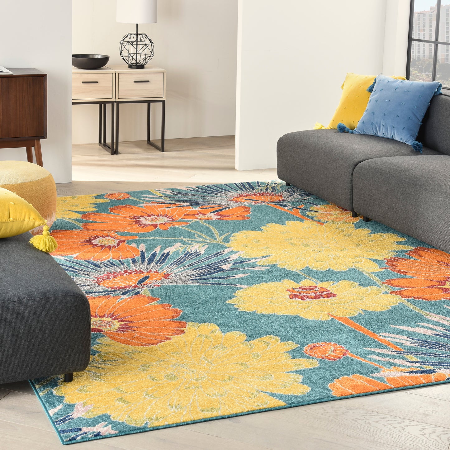 Vibrant floral area rug in teal with yellow & orange blooms, paired with a gray sectional & yellow/blue cushions.