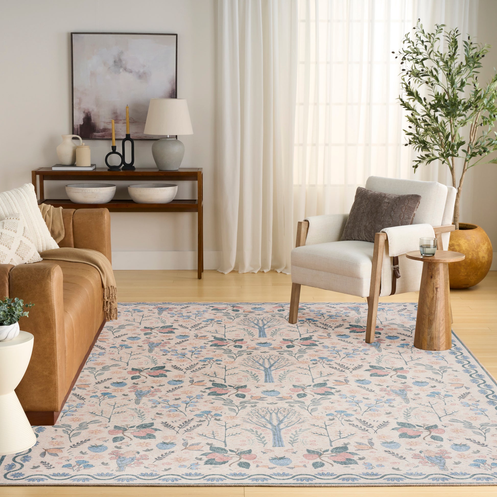 Cozy living room with blue-pink floral rug, brown leather sofa, white armchair, wooden console & side table, potted plant by sheer curtains.