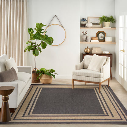 Neutral living room with striped beige armchair, gray sofa, tall plant, round wall hoop, woven baskets, beige rug.