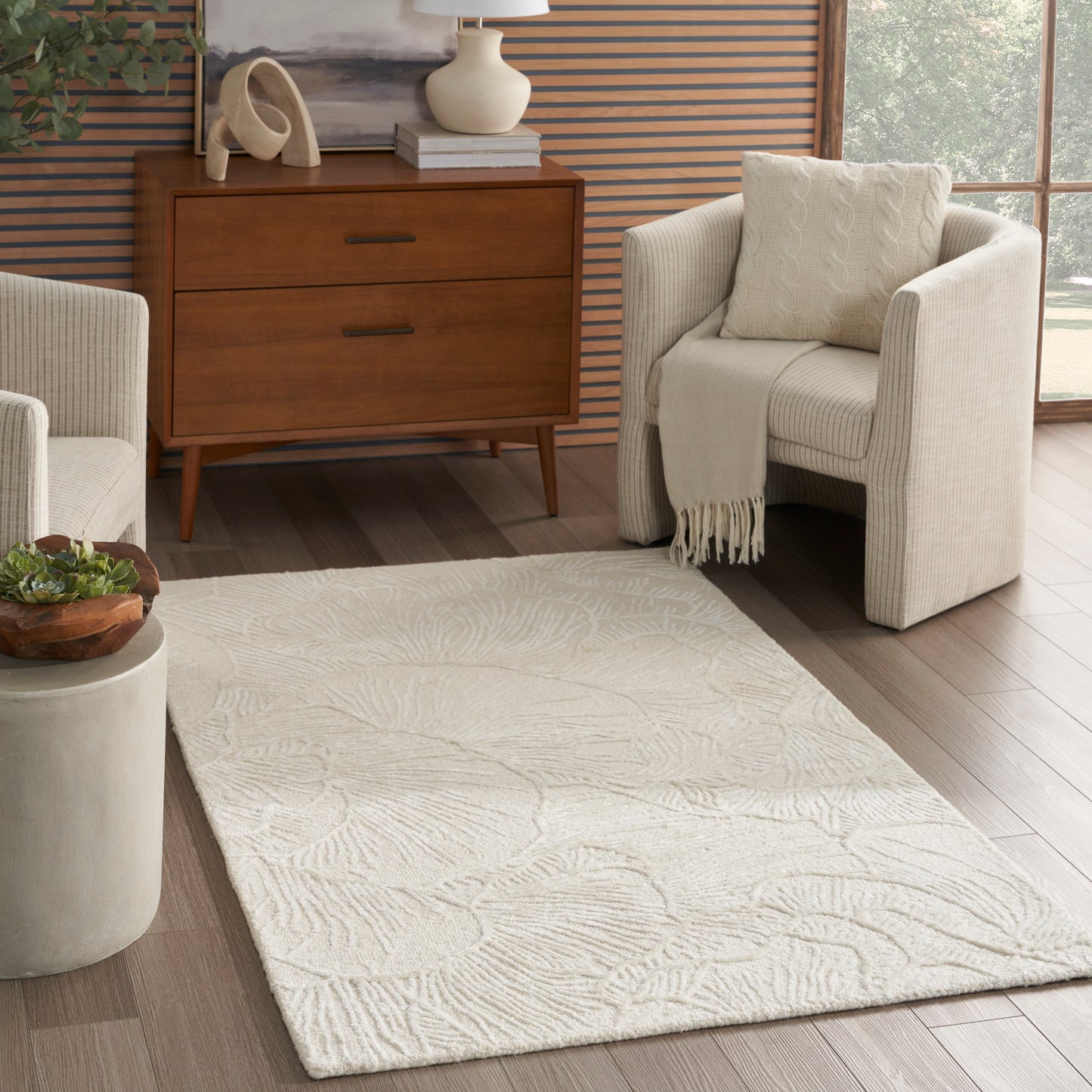 Beige textured area rug with a subtle leaf pattern on wood floor, paired with a mid-century dresser and cream chairs.