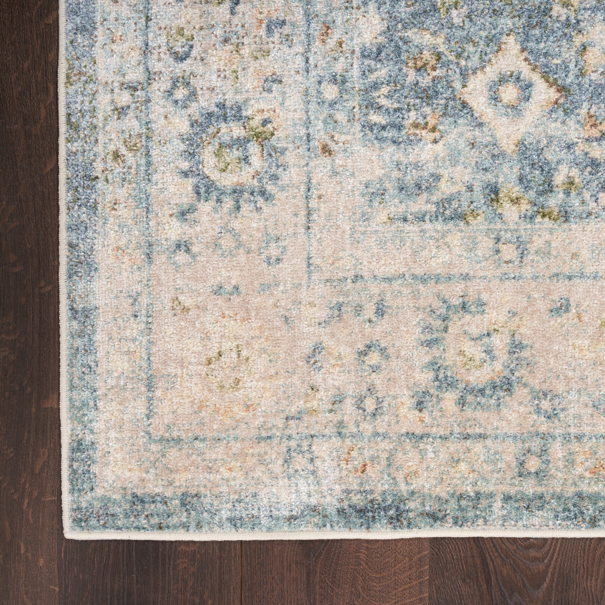 Rectangular woven rug in blue, ivory and tan with geometric/medallion motifs on dark wooden floor.