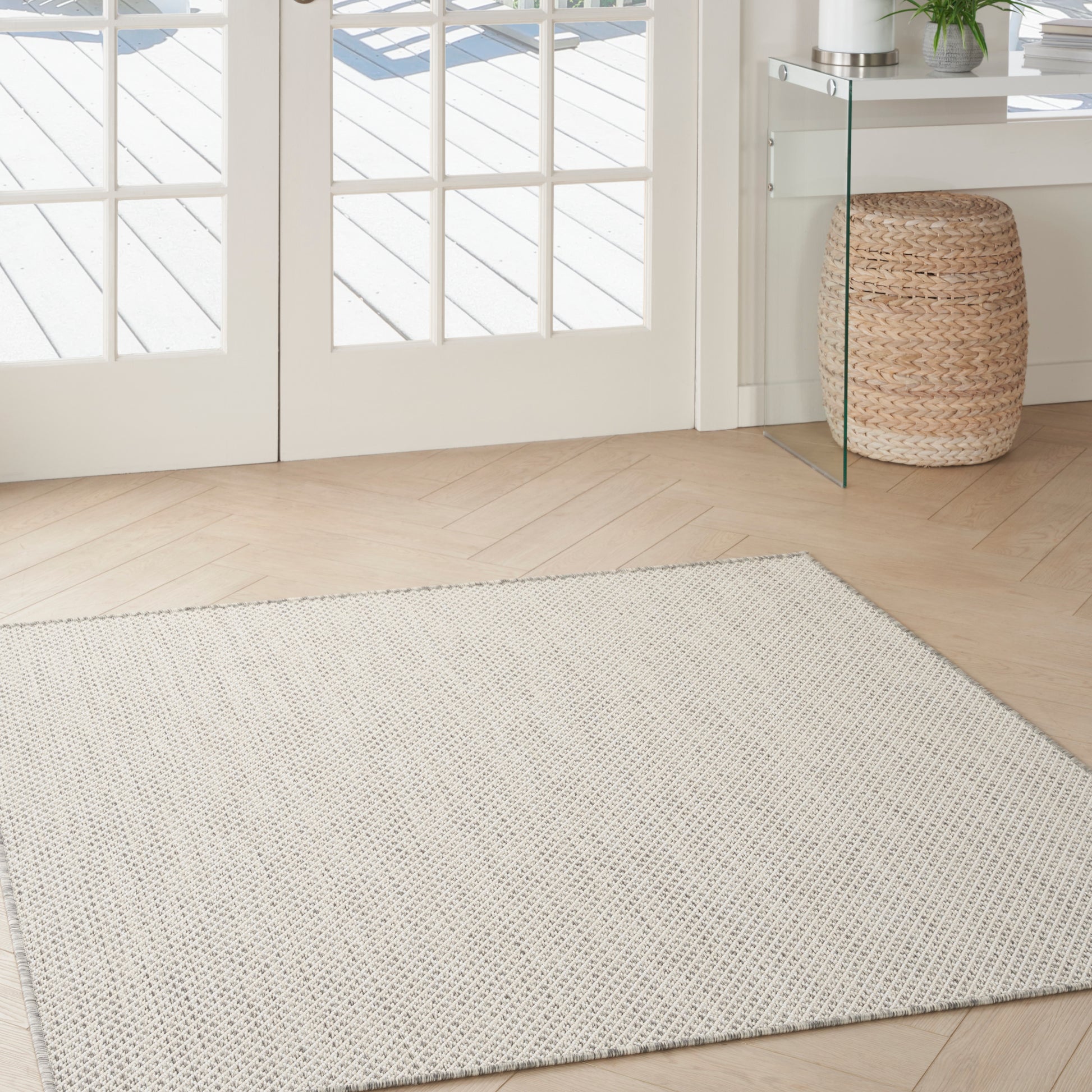 Light beige textured area rug on a light wood floor in an entryway with French doors and a woven basket.