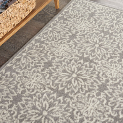 Grey rug with cream floral mandala pattern on wood floor, near wicker basket and wooden shelf.