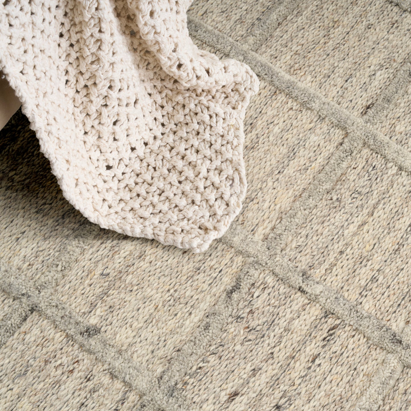 Beige textured rug with geometric lines, a cream chunky knit throw draped over it.
