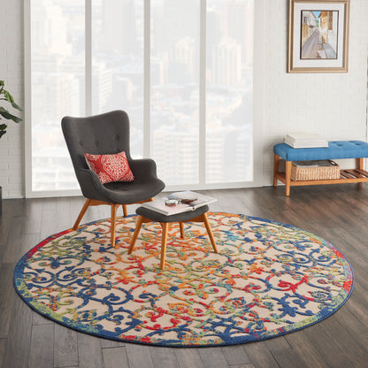 Round multicolor patterned rug under a gray mid-century armchair with wooden legs and ottoman in a bright city living room.